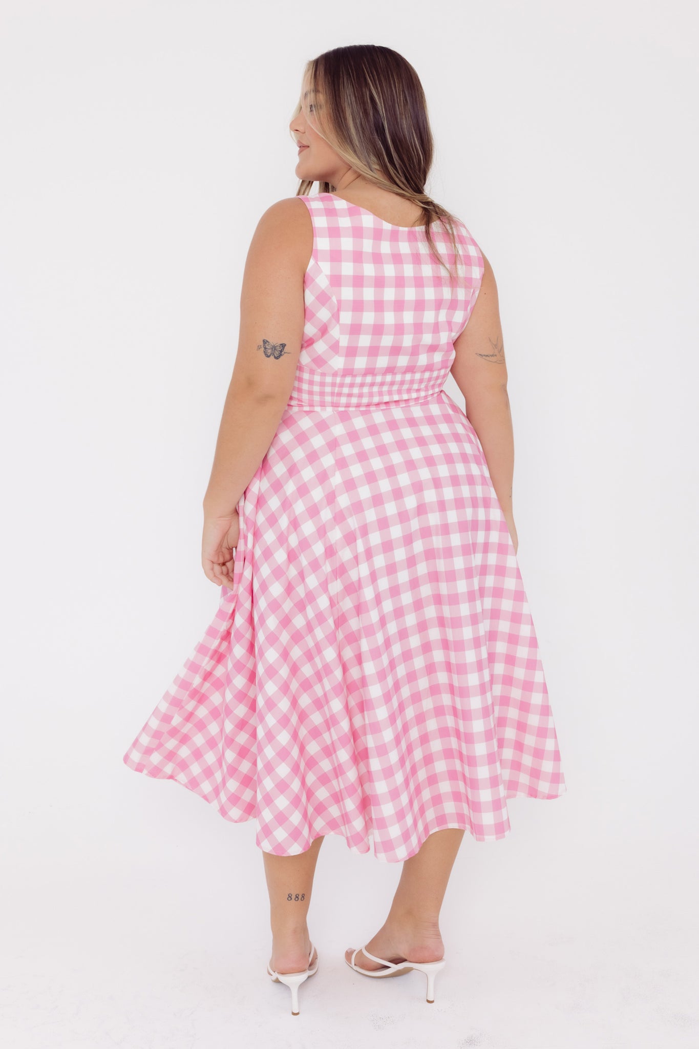 Back view of a woman wearing a Cherry Bobbins pink and white gingham cotton midi dress on a white background