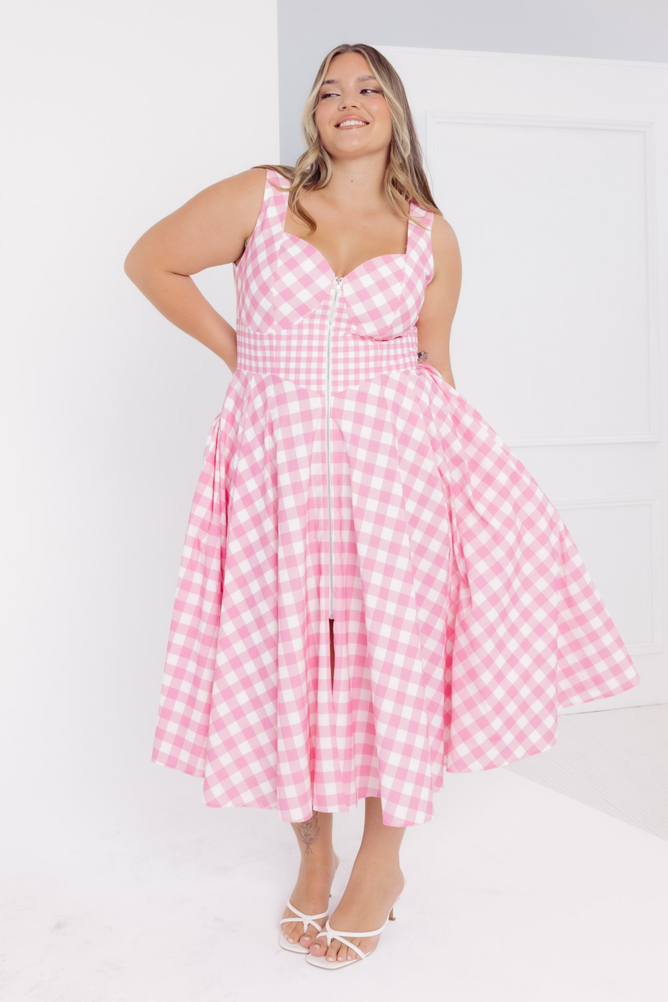 Front view of a woman wearing a Cherry Bobbins pink gingham cotton midi dress against a white background
