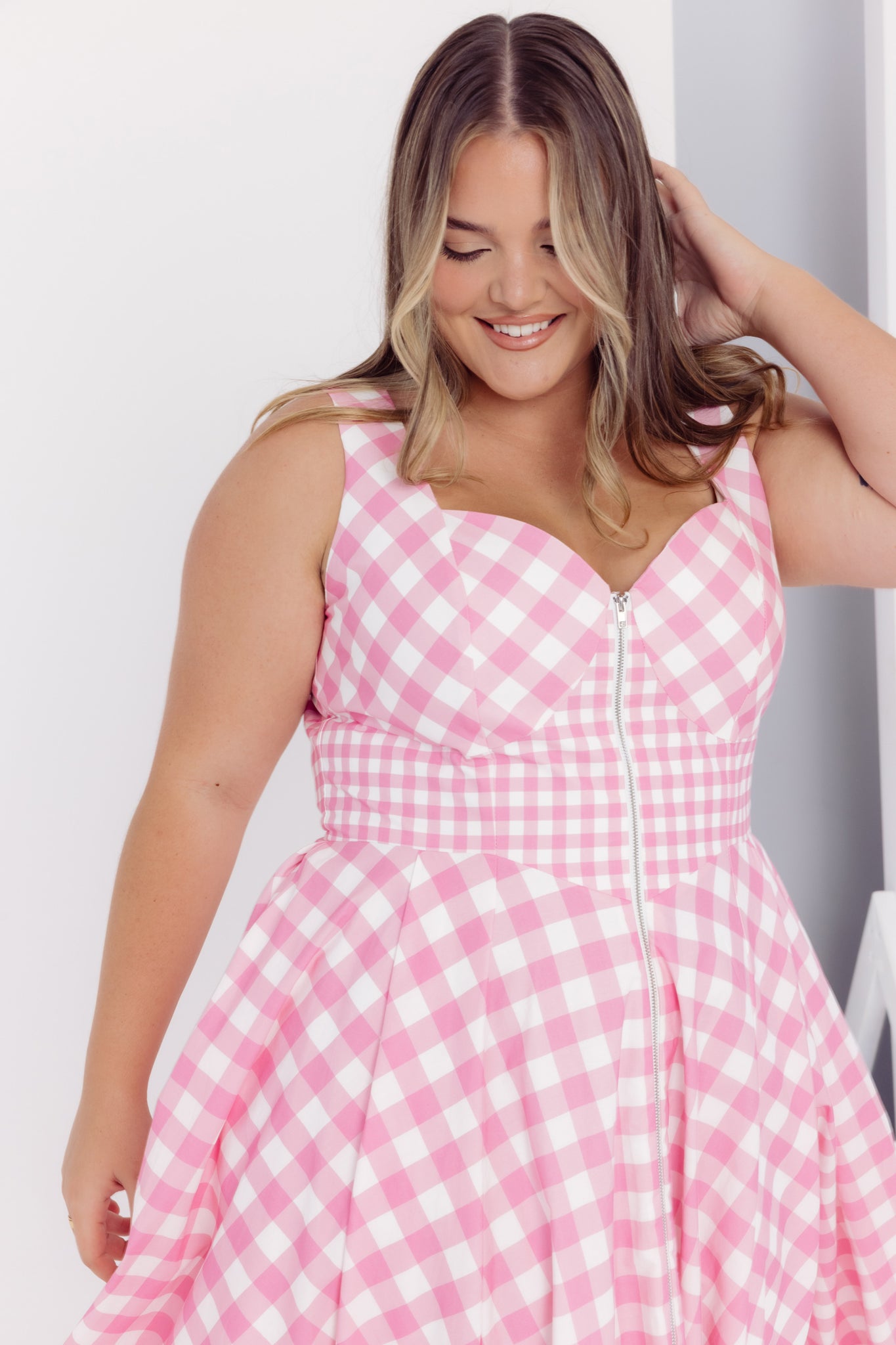 Cropped view of a woman wearing a Cherry Bobbins pink and white gingham midi cotton dress against a plain background