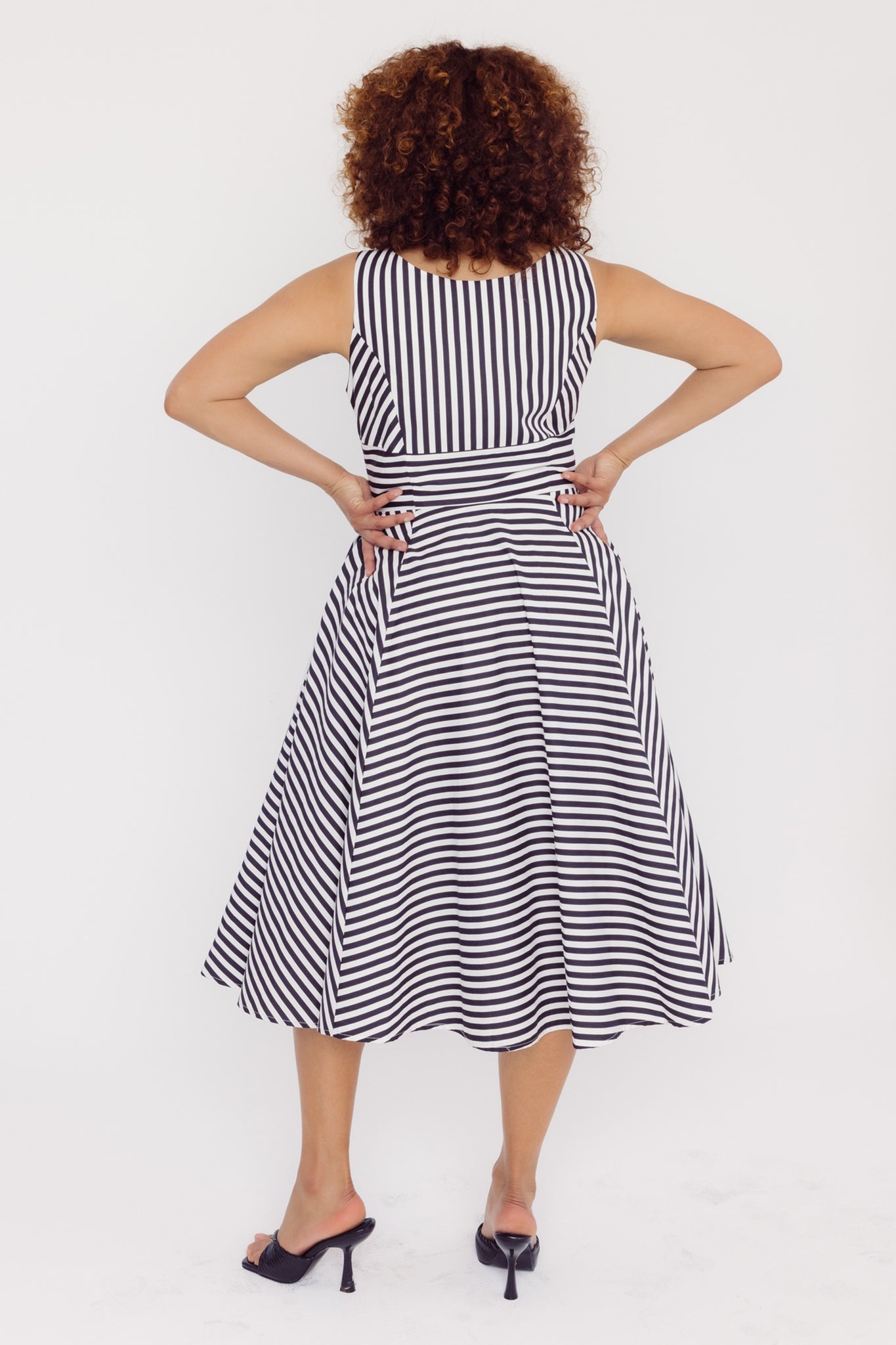 Back view of a woman wearing a Cherry Bobbins black and white striped cotton midi dress on a white background