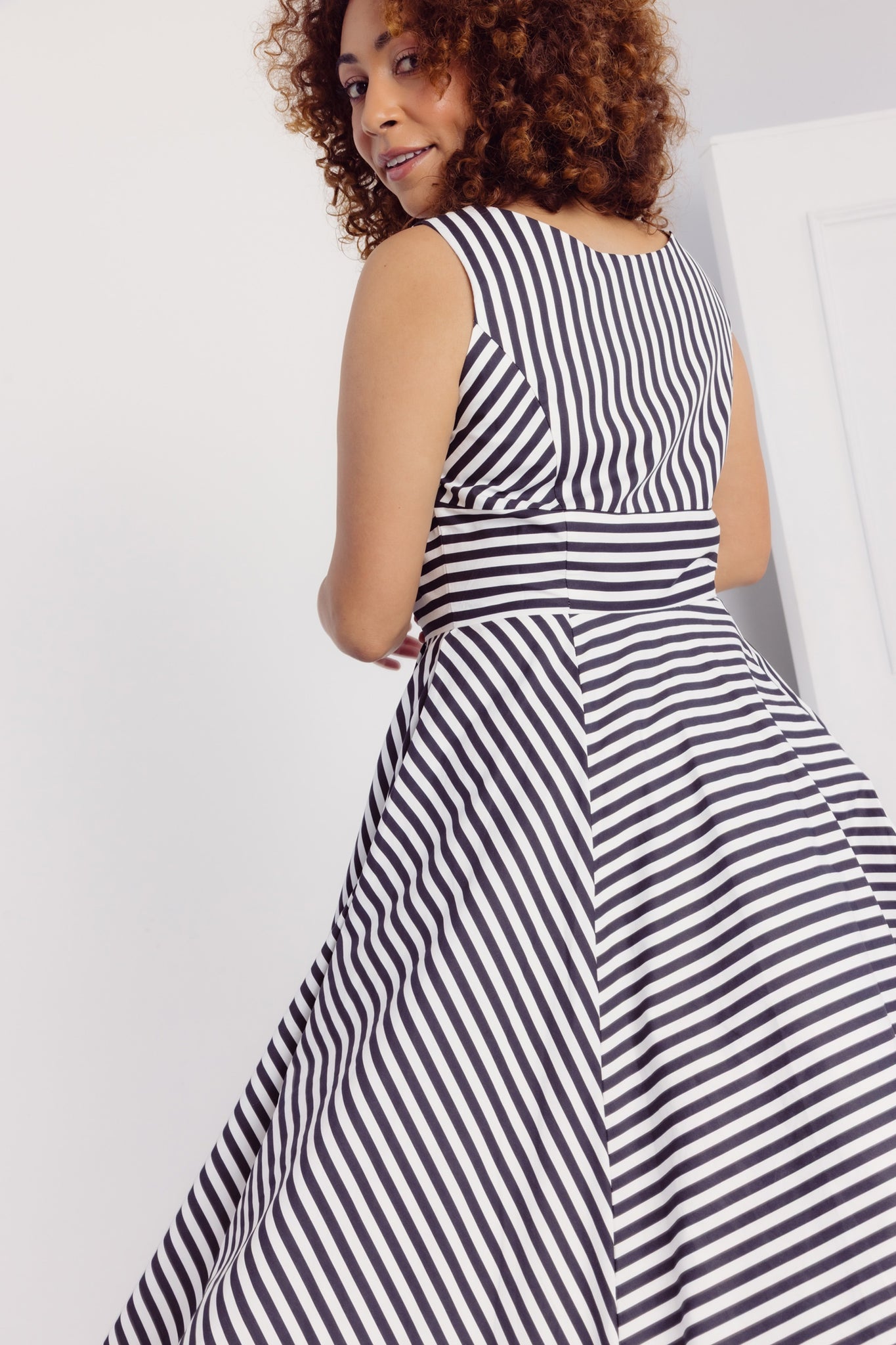 Close up image of the back of a woman wearing a Cherry Bobbins black and white striped cotton midi dress against a plain background