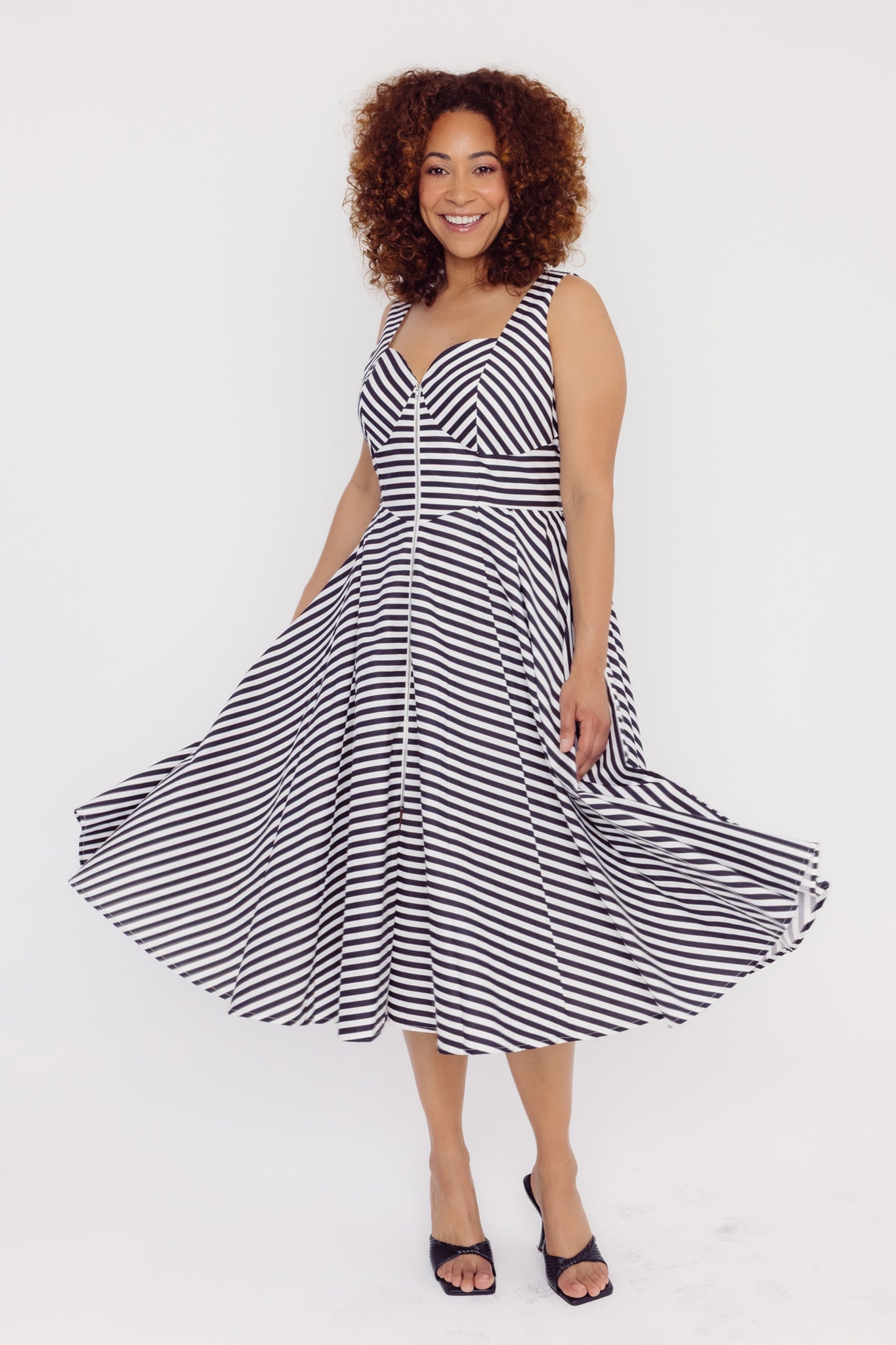 Front view of a woman wearing a Cherry Bobbins black and white striped cotton midi dress on a white background