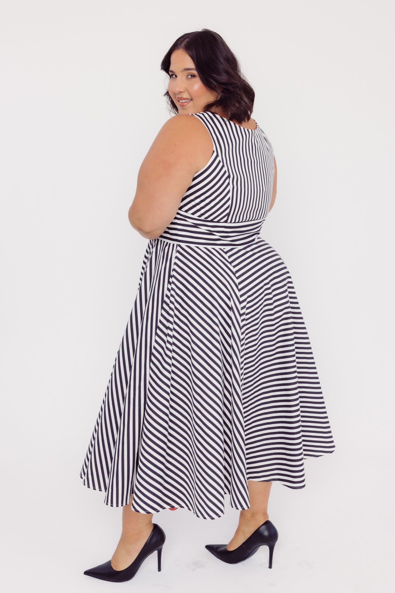Side back view of a plus size woman wearing a Cherry Bobbins black and white striped cotton midi dress on a white background