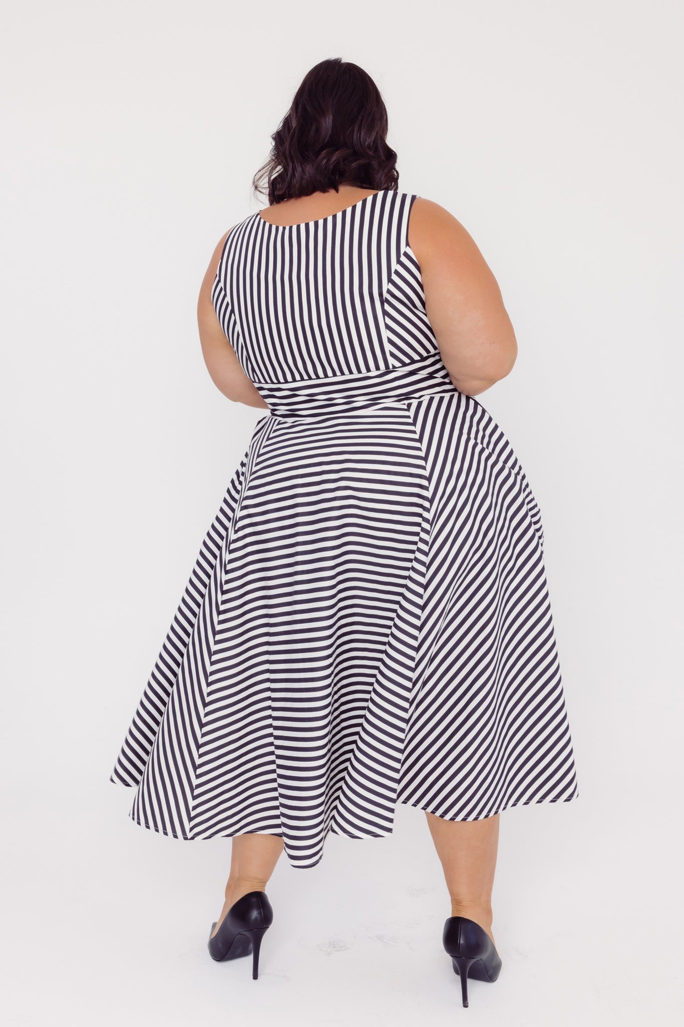 Back view of a plus size woman wearing a Cherry Bobbins black and white striped cotton midi dress on a white background