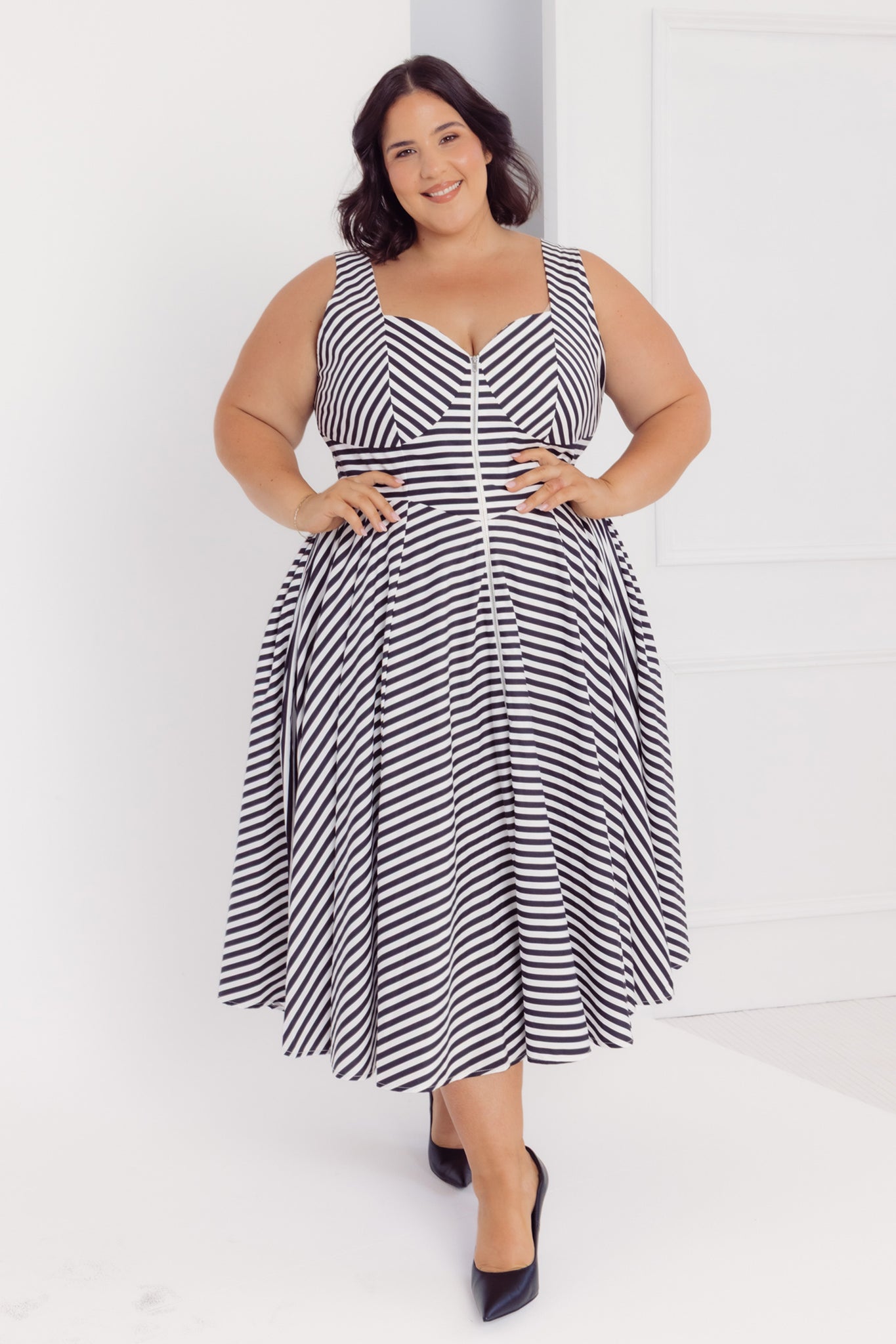 Front view of a plus size woman wearing a Cherry Bobbins black and white striped cotton midi dress against a white background