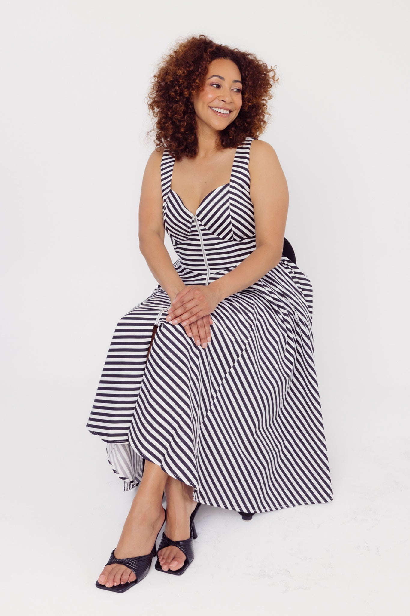 Woman sitting while wearing a Cherry Bobbins black and white striped cotton midi dress on a white background