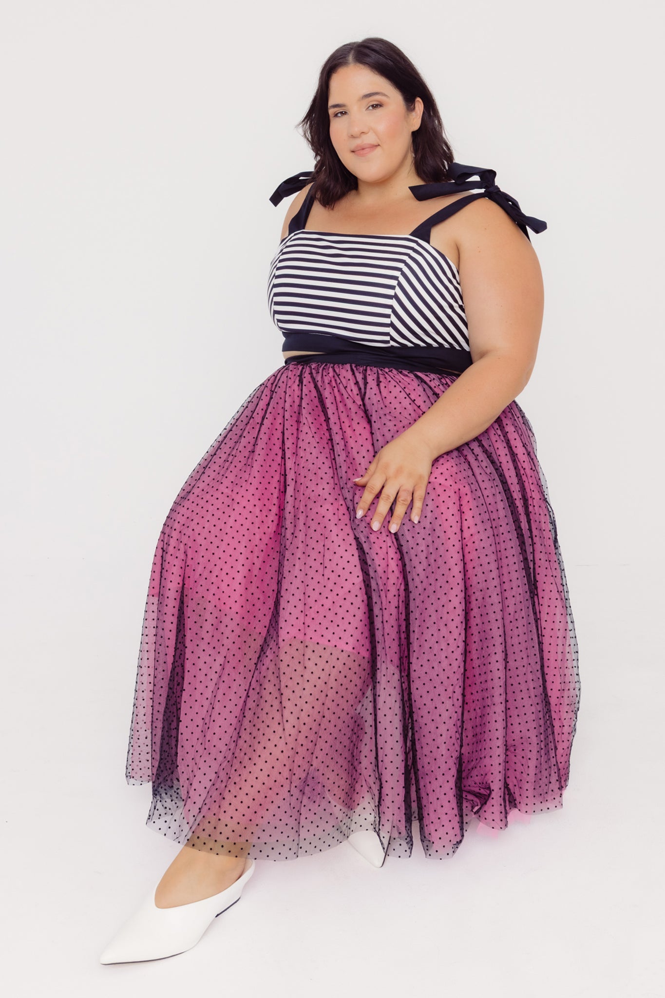 Woman wearing a Cherry Bobbins black and white striped cotton plus size top with a pink black polka dot tulle skirt on a white background