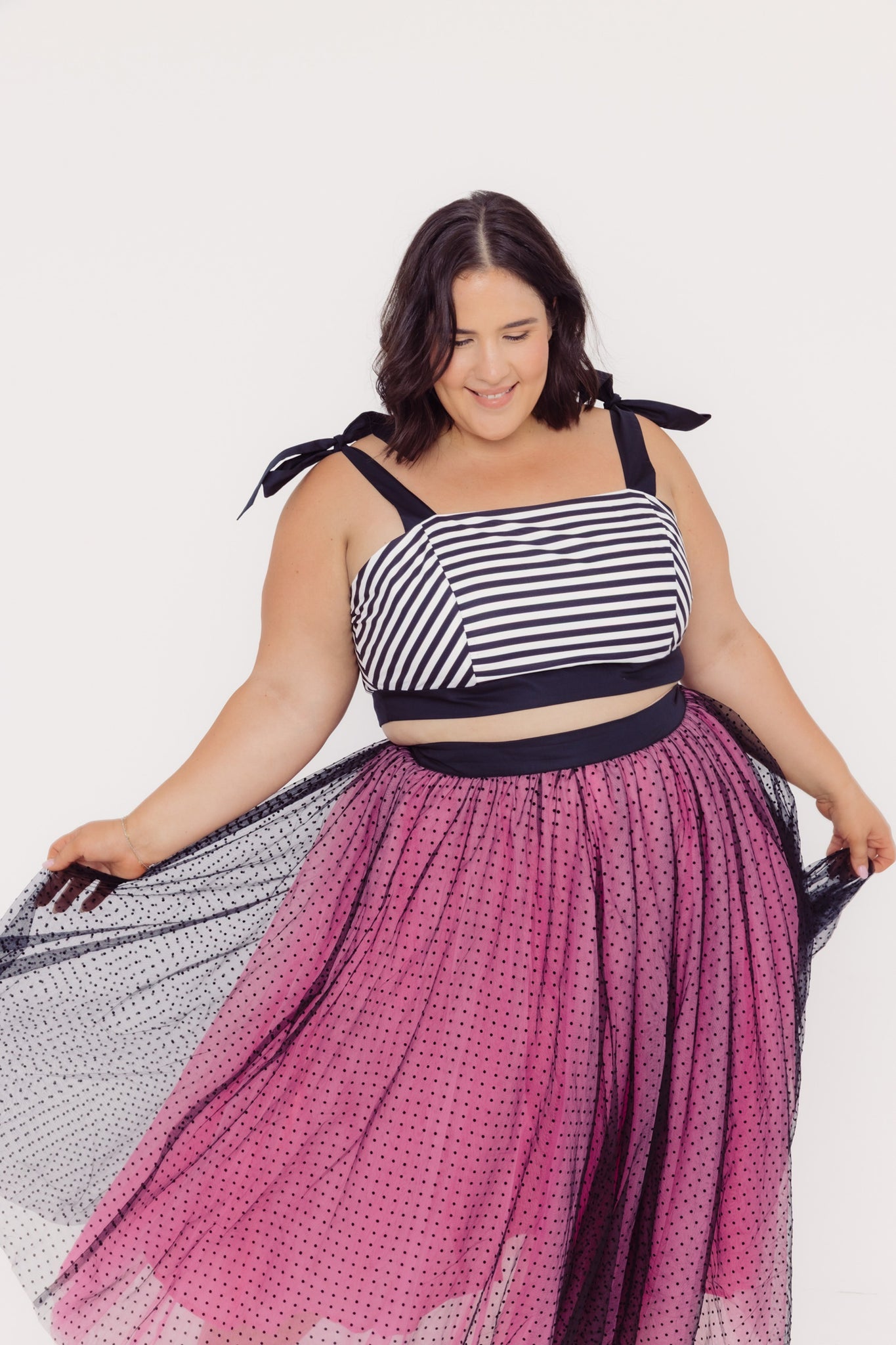 Front view of a plus size woman wearing a Cherry bobbins striped cotton top and twirling pink tulle skirt with a white background