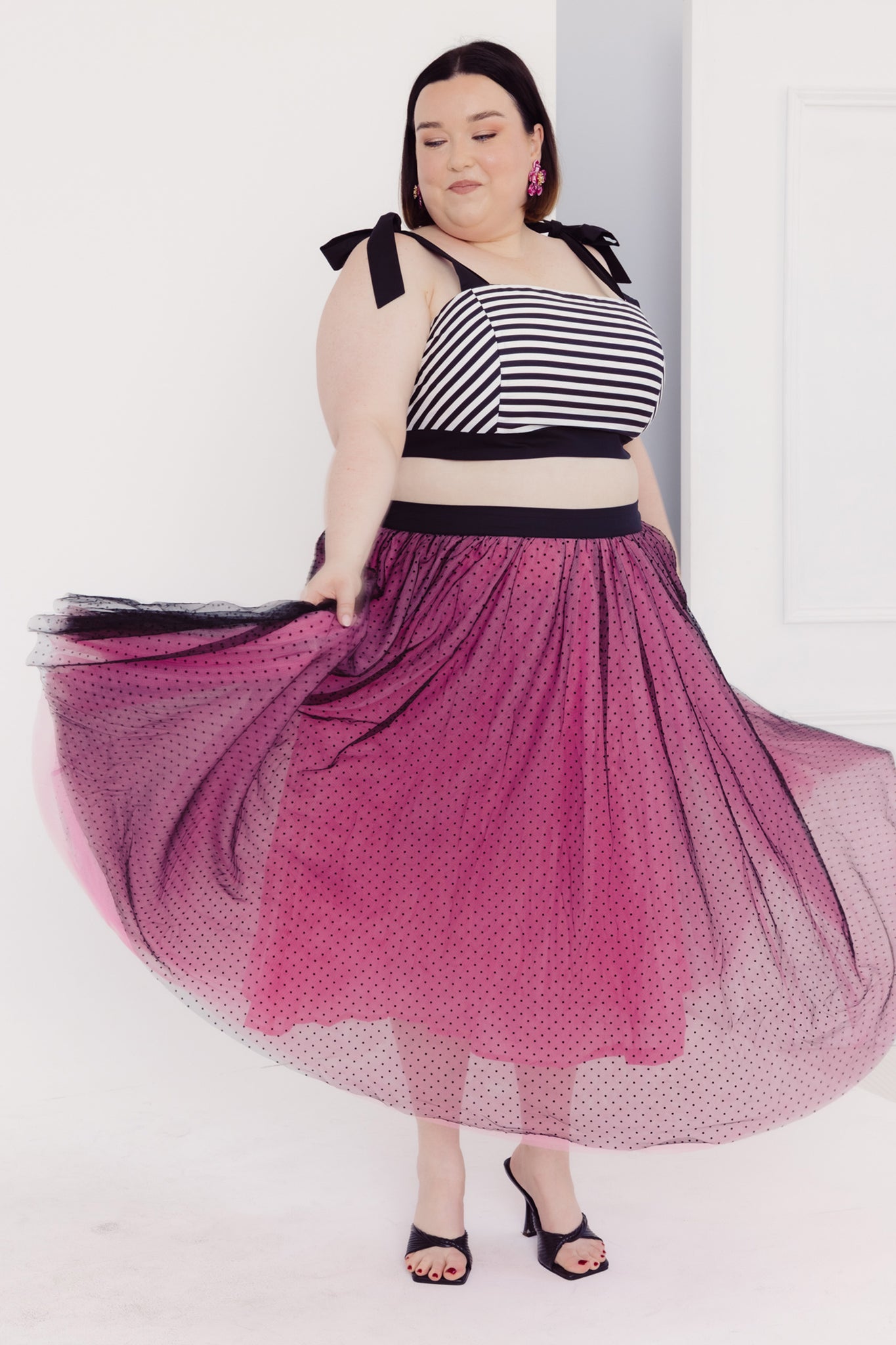 Woman twirling her skirt wearing a Cherry Bobbins striped cotton top and pink tulle skirt with black polka dots on a white background