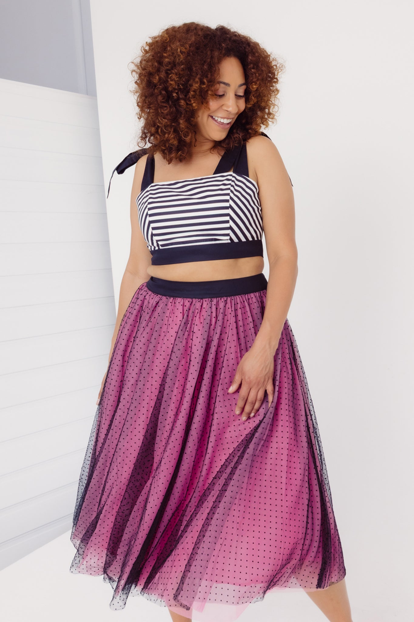 Front view of a woman wearing a Cherry Bobbins striped cotton crop top and a pink black tulle skirt with a white background