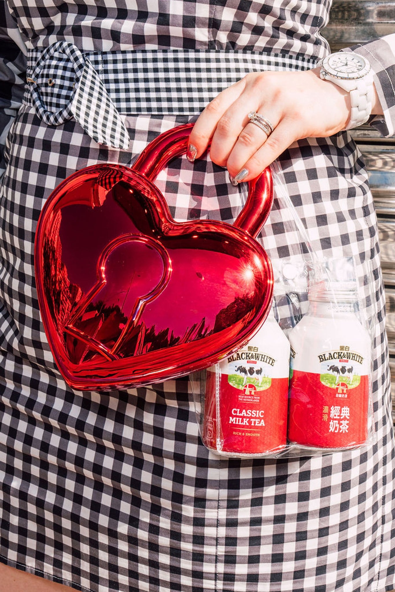 Person holding a red heart-shaped bag with two bottles of Black & White Classic Milk Tea in a transparent bag