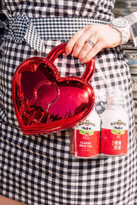 Person holding a red heart-shaped bag with two bottles of Black & White Classic Milk Tea in a transparent bag