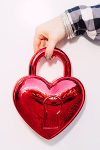 Red heart-shaped locket bag held by a hand on a white background