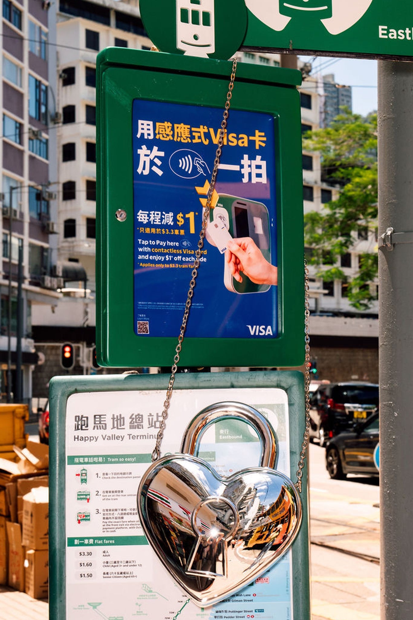 Street sign and tram schedule in Hong Kong with a silver heart-shaped locket bag hanging from it.