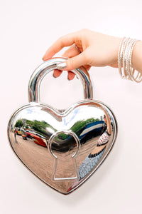 Heart-shaped silver locket handbag held by a hand on a white background
