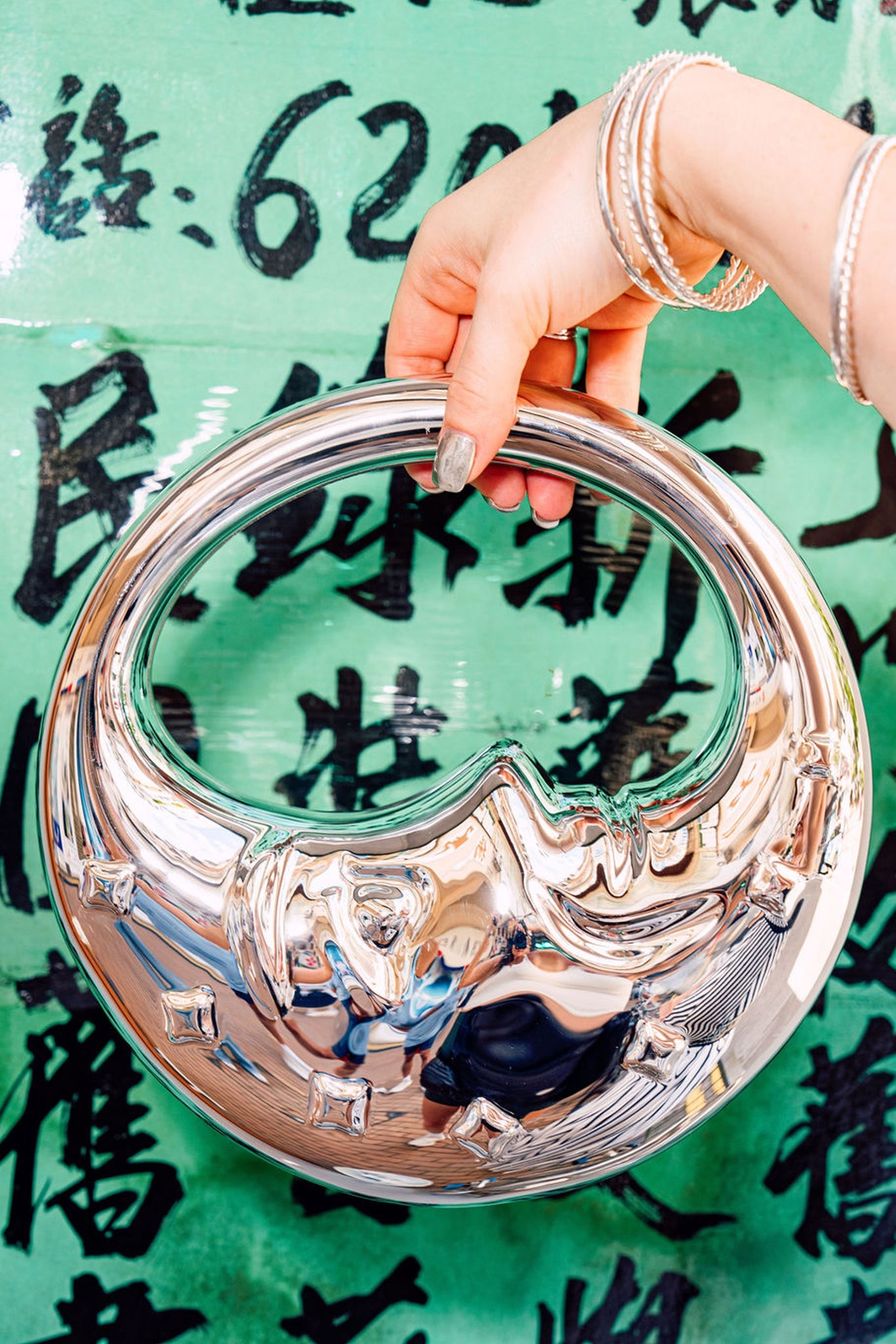 Hand holding a silver moon face bag against a green background with black text