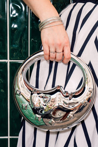 Person holding a silver moon face handbag, wearing a stripe Cherry Bobbins dress against a green tiled wall.