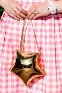 Person holding a gold handbag with a pink checkered Cherry Bobbins dress on