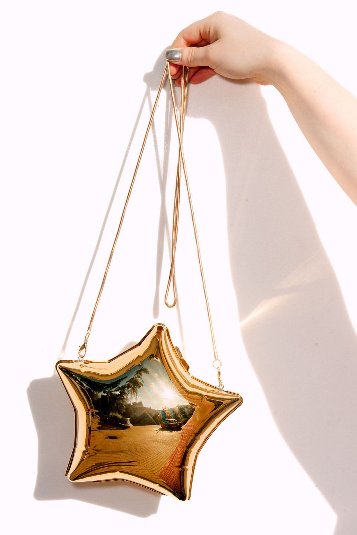Gold star-shaped handbag held by a hand against a white background
