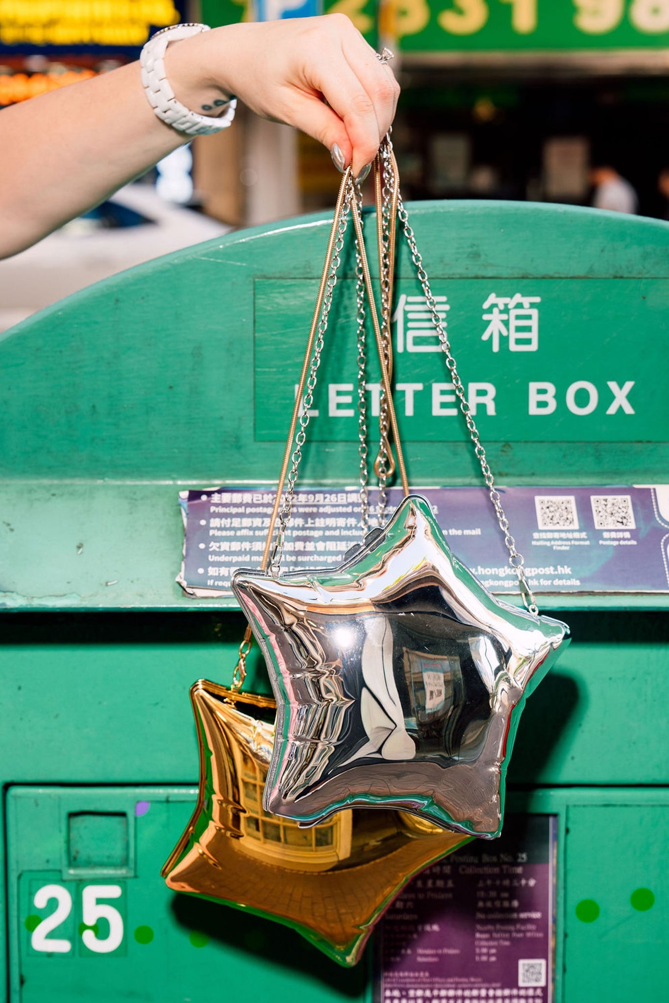 Star-shaped handbags in both gold and silver held above a green mailbox.