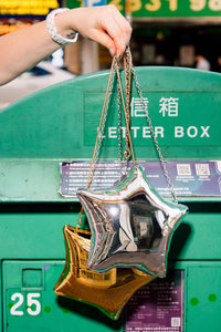 Star-shaped handbags in both gold and silver held above a green mailbox.