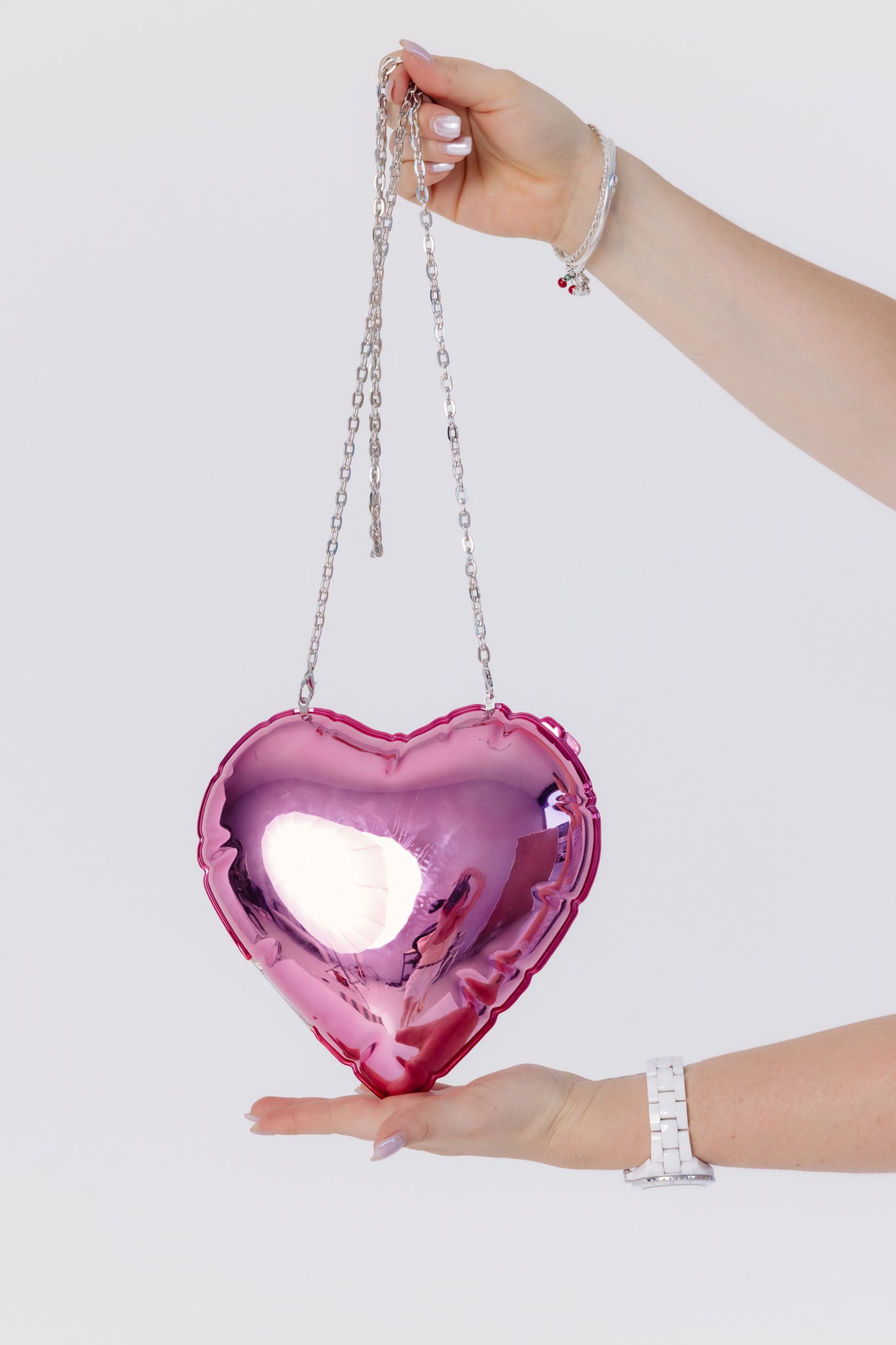 Heart-shaped pink mirror bag held by a hand on a white background