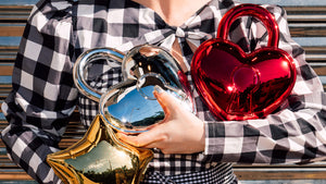 Person holding three metallic heart and star shaped reflective bags in red, gold, and silver in landscape